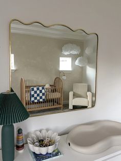 a mirror that is on the side of a wall above a dresser with a lamp