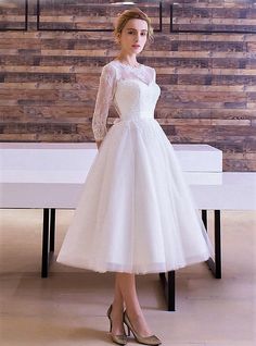 a woman standing in front of a table wearing a white dress with sheer sleeves and high heels