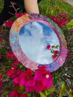 a person holding a mirror with flowers in front of it and the reflection of clouds