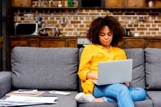 a woman sitting on a couch with a laptop computer in her lap and looking at the screen