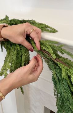 two hands are working on a wreath made out of fake fir branches and twine with scissors