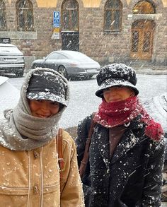 two women are standing in the snow with hats on and scarves over their heads