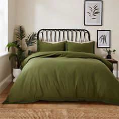 a bed with green sheets and pillows in a room next to a potted plant