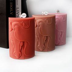 three different colored candles sitting next to each other in front of a book case with a horse on it