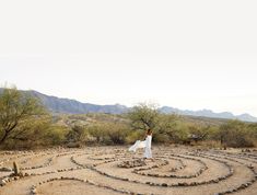 a woman standing in the middle of a circular stone maze with mountains in the background