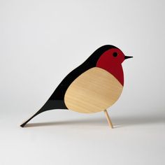 a small wooden bird sitting on top of a white table next to a black and red bird