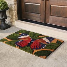 a door mat with a butterfly on it in front of a wooden door and planters