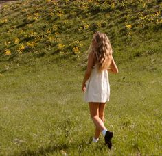 a woman in a white dress is walking through the grass with her hair blowing in the wind