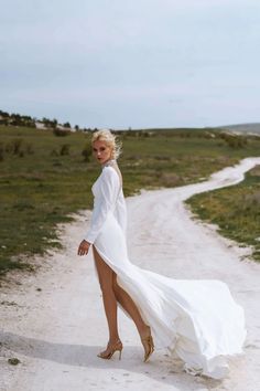 a woman in a white dress walking down a dirt road