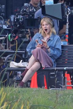 a woman sitting on top of a bench in front of a movie set with people behind her