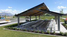 an empty picnic area with benches and tables in the grass near a parking lot on a sunny day