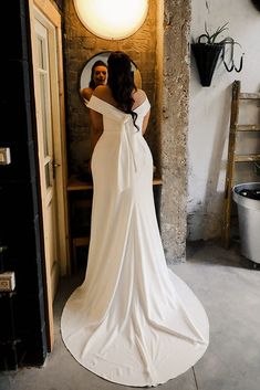 a woman standing in front of a mirror wearing a white dress