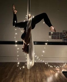 a woman doing aerial acrobatic tricks on a pole with lights around her