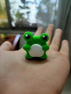 a small green frog toy sitting on top of someone's hand in front of a tv