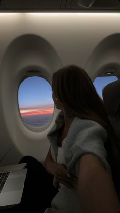 a woman sitting in an airplane looking out the window at the sunset and clouds outside