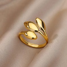 a gold ring sitting on top of a white cloth covered surface with two leaves in the middle