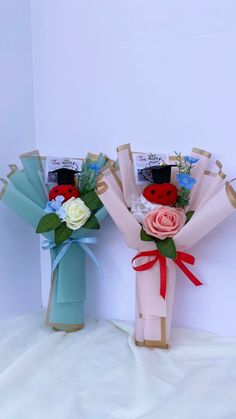 two vases with flowers in them sitting on a white cloth covered surface, one is blue and the other is pink