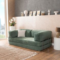 a green couch sitting on top of a hard wood floor next to a white rug