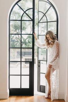 a woman standing in front of an open door wearing a white lace dress and high heels