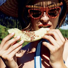 a woman wearing sunglasses and a straw hat eating a piece of food with her hands