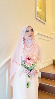 a woman wearing a hijab and holding a bouquet of flowers in her hand