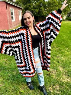 a woman is standing in the grass wearing a crocheted jacket