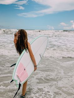 a woman standing in the ocean holding a surfboard with a pink fish on it