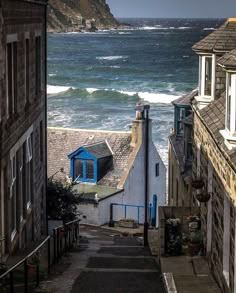 an alley way leading to the ocean with houses on either side and waves crashing into the shore