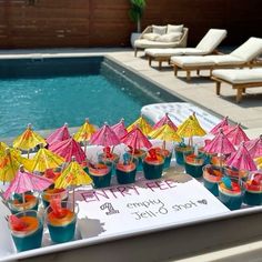 there are many cupcakes with umbrellas on the table next to the pool