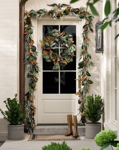 a white front door with a wreath on the side and boots next to it, in front of some potted plants