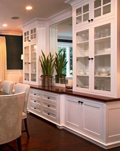 a dining room table and chairs in front of white cupboards with glass doors on them