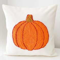 an orange pumpkin embroidered onto a white pillow