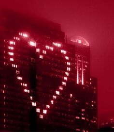 the city is lit up at night with red light in the windows and skyscrapers