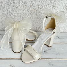 a pair of white high heeled shoes with pearls on the toes and bows at the ankle