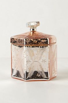 a glass jar with an intricate design on the front and sides, sitting on a white surface