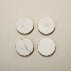 four white marble coasters sitting on top of a beige tablecloth covered flooring