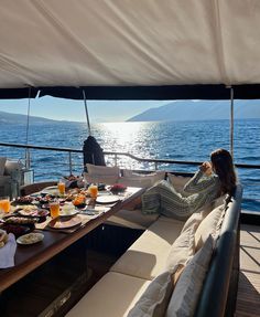 a woman sitting at a table on top of a boat with food and drinks in front of her