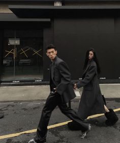 two people are walking down the street in front of a building with black doors and windows