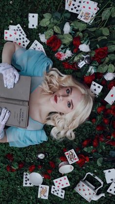 a woman laying on the ground surrounded by playing cards and roses, holding a box