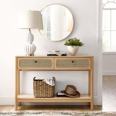 a wooden table topped with a mirror next to a lamp and a wicker basket