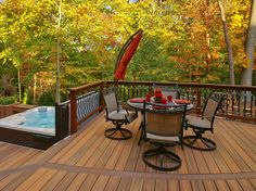 a deck with chairs, table and hot tub in the middle surrounded by wooded area