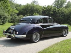 an old black car is parked on the side of the road