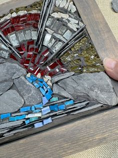 a person is holding a piece of art made out of rocks and glass mosaics