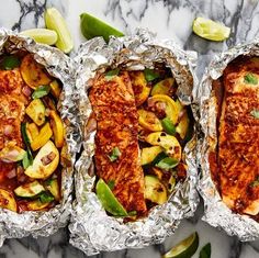 three foil packets filled with food on top of a marble countertop next to lime wedges