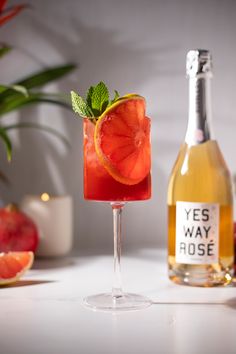 a glass filled with a drink next to a bottle of wine and some orange slices