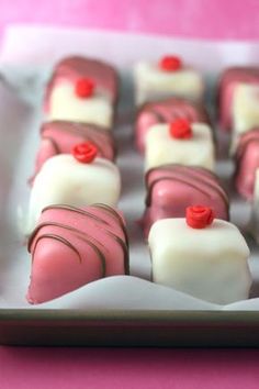 there are many pink and white desserts on the tray with red bows around them