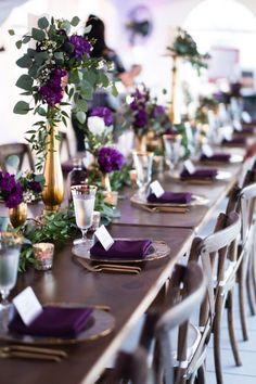 a long table with purple flowers and place settings