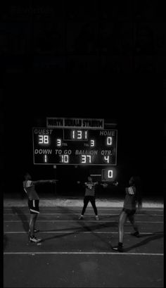 three people standing in front of an electronic scoreboard on a tennis court at night