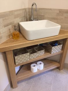 a bathroom sink sitting on top of a wooden counter next to two rolls of toilet paper