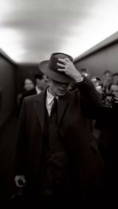 a man in a suit and hat walking down a hallway with other people behind him